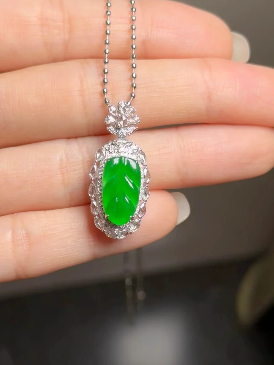Natural Type A jadeite leaf pendant in full vivid green, set in 18K white gold with small white stones, held in the hand (still from the product video)